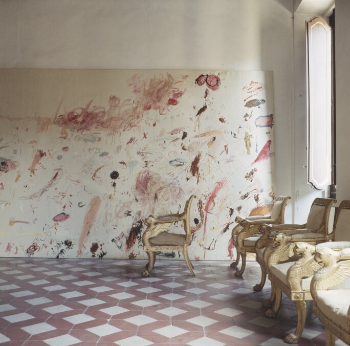 Room in the Rome apartment of artist Cy Twombly featuring a row of French Empire chairs and one of Twombly's paintings leaning against the back wall.
