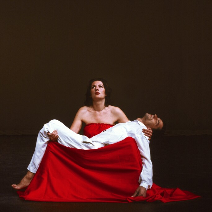 Ulay, in white, laying across Marina Abramavics lap, as she is dressed in red.jpg