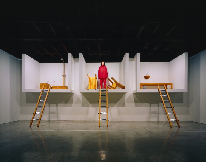 Marina Abramović dressed in red standing in one of three elevated rooms during her performance piece at Sean Kelly gallery in New York in 2002.jpg